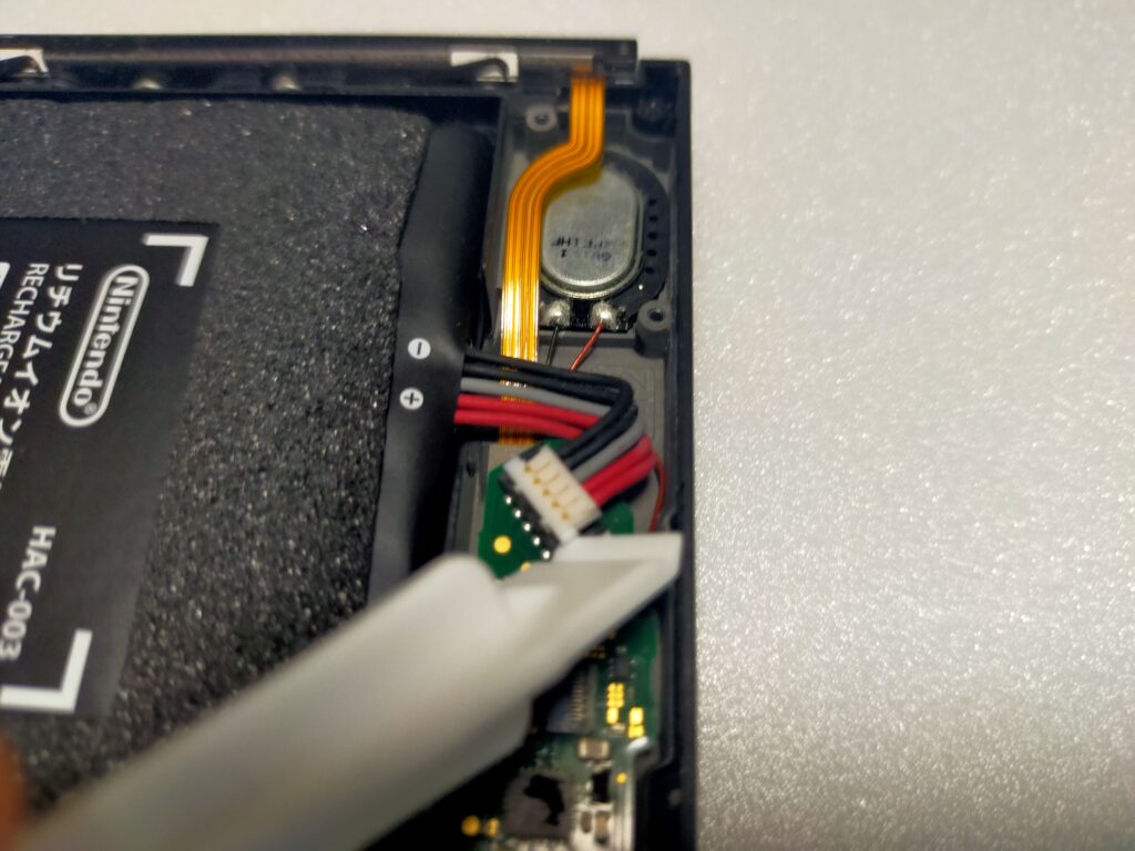 ヘラで持ち上げられた任天堂Switchのバッテリーのコネクター部分